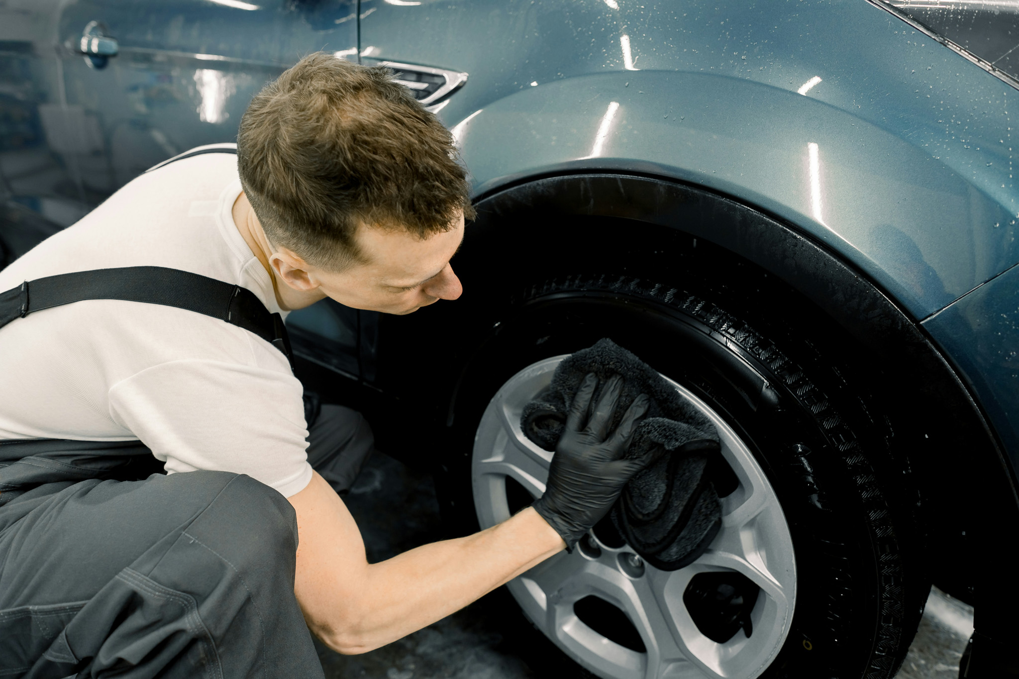 This image shows a technician wiping down the wheel on a car for the finishing touches of a job.